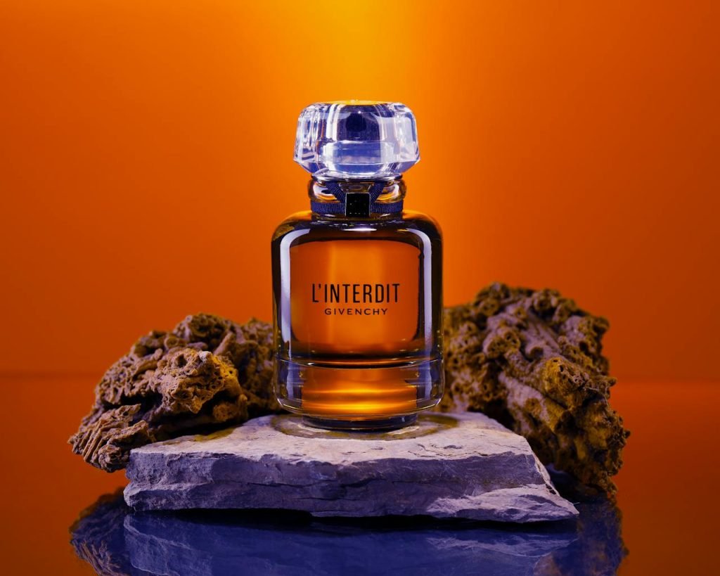 LInterdit perfume bottle displayed on rocks with vibrant orange background, Puebla, Mexico.